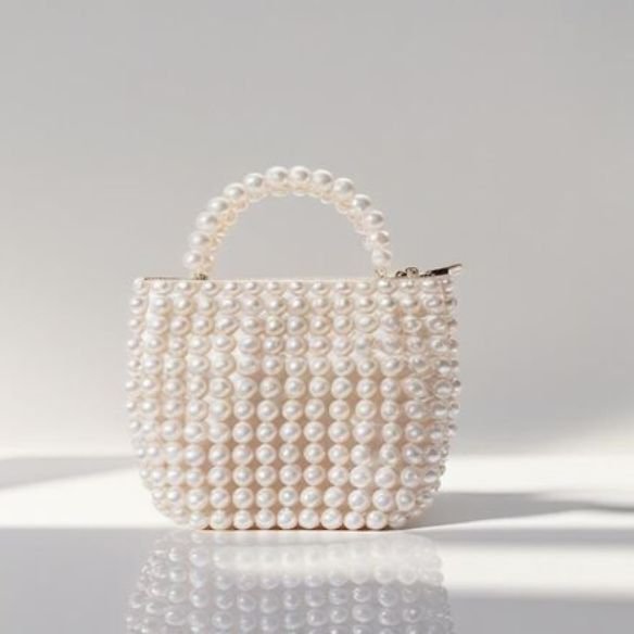 White pearl-covered handbag with pearl handle casting soft shadow on white surface, featured accessory from bead&blush.store’s elegant collection.